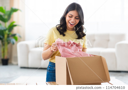 A muslim woman appears delighted as she unpacks an article of pink clothing from a box in her home A muslim woman appears delighted as she unpacks an article of pink clothing from a box in her home 114704610