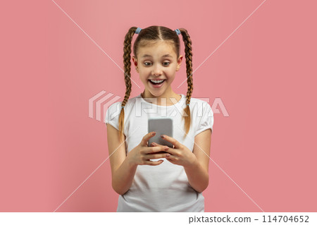 Young caucasian girl expressing amazement at smartphone content, isolated on pink background with a vibrant teen expression Young caucasian girl expressing amazement at smartphone content, isolated on pink background with a vibrant teen expression 114704652