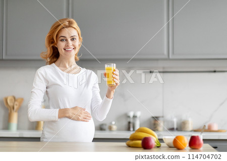 Bright european pregnant lady drinks orange juice in kitchen, emphasizing the value of vitamin C for prenatal nutrition 114704702