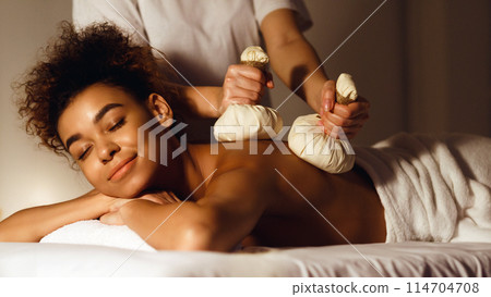 Thai herb compress massage. Woman relaxing in beauty spa, lying with closed eyes Thai herb compress massage. Woman relaxing in beauty spa, lying with closed eyes 114704708