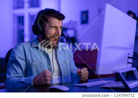 A millennial guy's intense reaction exemplifies the emotional highs and lows of gaming at home, showcasing the potential for addiction within the gamer culture A millennial guy's intense reaction exemplifies the emotional highs and lows of gaming at home, showcasing the potential for addiction within the gamer culture 114704732