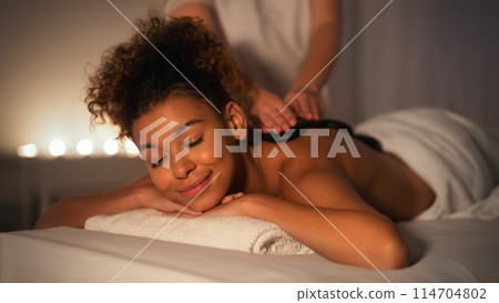 Captured in a softly lit setting, an African American lady appears tranquil during a spa massage session focused on relaxation and wellbeing 114704802