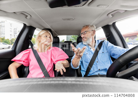 An older couple seems to be in a disagreement while the man is driving and the woman looks disapprovingly 114704808
