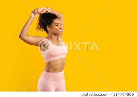 An african american woman performs a stretch displaying flexibility and strength, isolated on a yellow background for a fitness theme An african american woman performs a stretch displaying flexibility and strength, isolated on a yellow background for a fitness theme 114704809