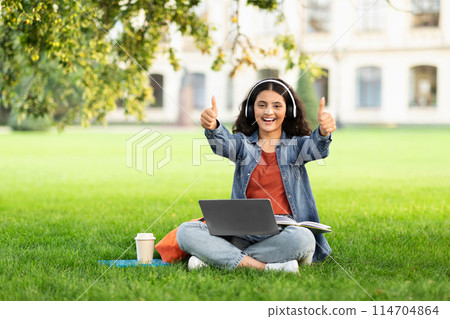 An Indian woman student gives thumbs up while using her laptop on a campus lawn, a sign of positive education experiences An Indian woman student gives thumbs up while using her laptop on a campus lawn, a sign of positive education experiences 114704864