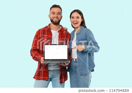Enthusiastic couple holding a laptop with a blank screen, great for mockup, isolated on a blue backdrop 114704889