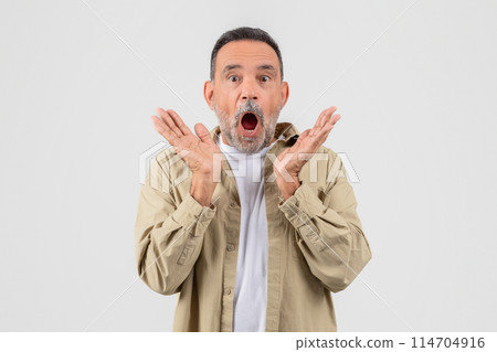Shocked elderly man with raised hands and an open mouth expressing surprise, isolated on a white background Shocked elderly man with raised hands and an open mouth expressing surprise, isolated on a white background 114704916
