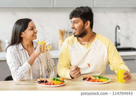 An eastern millennial couple enjoys a light-hearted moment with a toast of orange juice in their kitchen, expressing joy and love 114704943