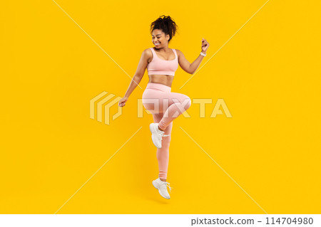 An energetic african american lady happily hopping, portraying a sense of joy and fitness, isolated against an eye-catching yellow background 114704980