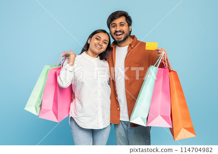 Excited young Indian couple with colorful shopping bags, expressing pleasure from a successful shopping spree 114704982