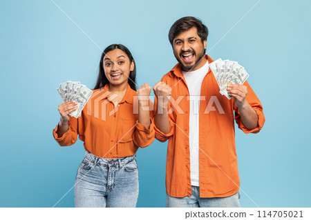 Indian man and woman excitedly holding and displaying cash, symbolizing financial success or win on blue 114705021