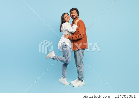 A loving Indian couple enjoys a close embrace while playfully lifting one leg, portraying affection 114705091