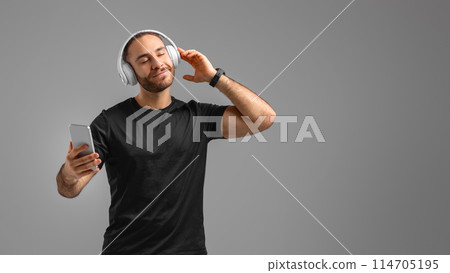 Relaxed man in activewear enjoys music on his smartphone, embodying leisure and enjoyment, using headphones 114705195