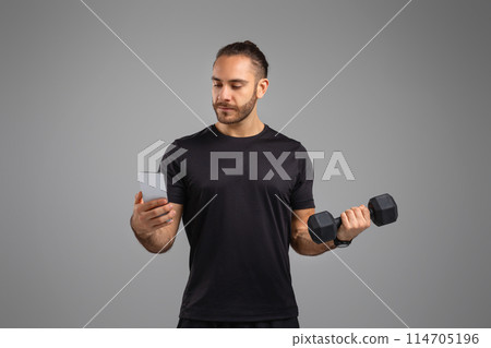 A man lifts a dumbbell while simultaneously checking his smartphone, illustrating fitness mobile app A man lifts a dumbbell while simultaneously checking his smartphone, illustrating fitness mobile app 114705196