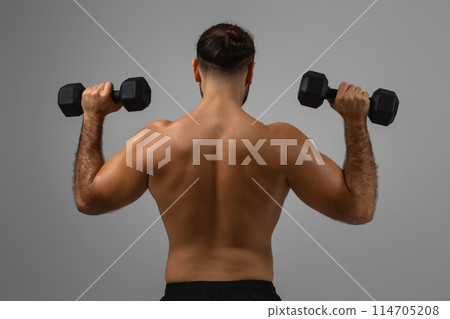 A muscular man's back is on display as he performs an exercise with black dumbbells against a grey backdrop 114705208
