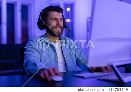 Content bearded man gamer wearing headset enjoys gaming in a neon-lit room with dedicated focus at home 114705249