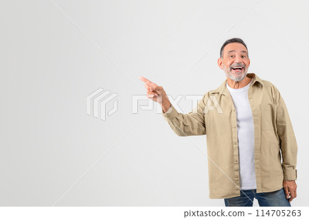 Smiling older man confidently pointing to the side, gazing away as if introducing something on a white background 114705263