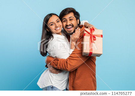 Eastern man and woman share a happy moment as they embrace with a gift box, symbolizing giving and affection 114705277