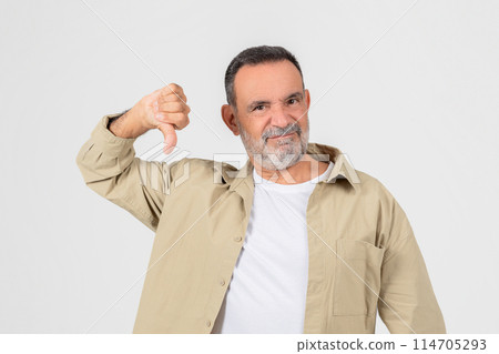 Disgruntled older man with a beard giving a thumbs down sign, signifying disapproval or dissatisfaction on white backdrop 114705293
