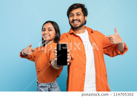 Indian couple smiling confidently while pointing thumbs at a smartphone, perfect for technology ads 114705302