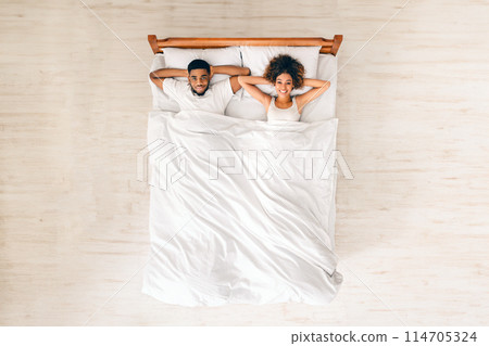 Happy married black couple resting in bed, lying with hands behind head after waking up in morning, top view 114705324