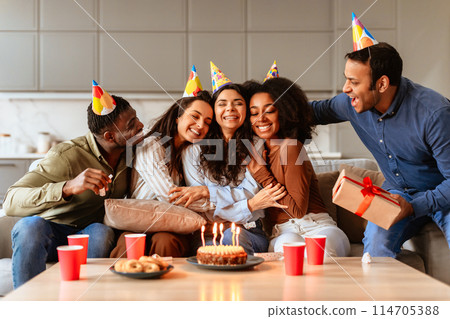 Multiracial friends embrace and enjoy the festivities of a birthday party celebration in a home setting 114705388