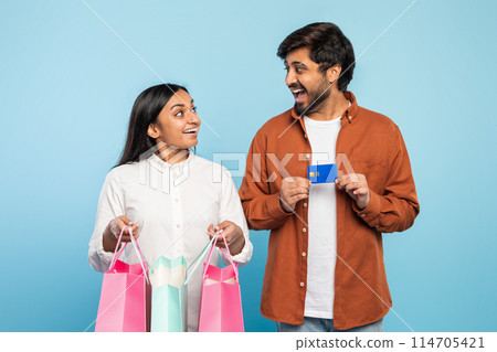 Indian man and woman happily hold shopping bags and a credit card, symbolizing consumerism and leisure Indian man and woman happily hold shopping bags and a credit card, symbolizing consumerism and leisure 114705421