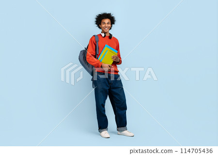 Casual dressed young african american man holding books with a backpack on a blue background Casual dressed young african american man holding books with a backpack on a blue background 114705436