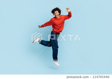 Joyful young african american man with curly hair jumping in mid-air expressing elation 114705440