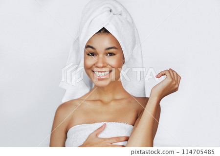Smiling afro-american girl with naked shoulders and towel on head in spa. Happy spa day concept Smiling afro-american girl with naked shoulders and towel on head in spa. Happy spa day concept 114705485