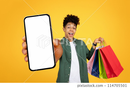 Laughing young black man holding out a smartphone with a mockup screen and shopping bags Laughing young black man holding out a smartphone with a mockup screen and shopping bags 114705501