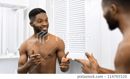 A bare-chested African american man gives a thumbs-up to his reflection, symbolizing self-satisfaction and a positive self-image A bare-chested African american man gives a thumbs-up to his reflection, symbolizing self-satisfaction and a positive self-image 114705520
