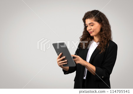Businesswoman engaged with a digital tablet, possibly reviewing reports or browsing 114705541