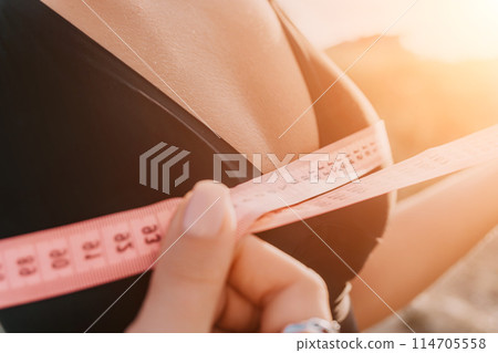 A woman is holding a pink tape measure and is measuring her breasts after morning fitness A woman is holding a pink tape measure and is measuring her breasts after morning fitness 114705558