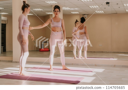 Well looking middle aged sporty woman, fitness instructor in pink sportswear doing stretching and pilates on yoga mat in the studio with mirror. Female fitness yoga. Healthy lifestyle and harmony. Well looking middle aged sporty woman, fitness instructor in pink sportswear doing stretching and pilates on yoga mat in the studio with mirror. Female fitness yoga. Healthy lifestyle and harmony. 114705685