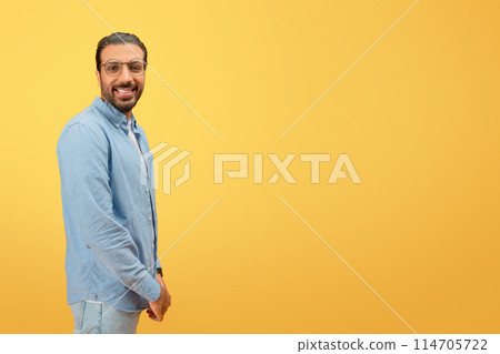 Confident and cheerful indian man with glasses and beard posing against a yellow background 114705722