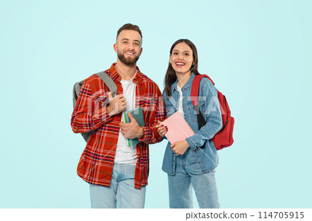 Two happy students man and woman standing with backpacks and books against blue backdrop, smiling to camera, representing concept of modern university life and study. Studio shot 114705915