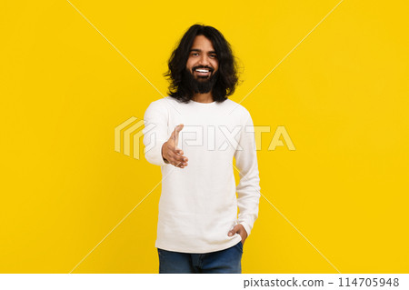 Friendly handsome long-haired bearded millennial indian guy outstretching hand and smiling at camera, greeting friend, meeting someone, isolated on yellow studio background 114705948