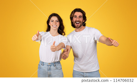 Radiant european couple giving thumbs up, displaying approval and happiness, dressed in white tees and denim, with joyful expressions on a cheerful yellow background, studio 114706032