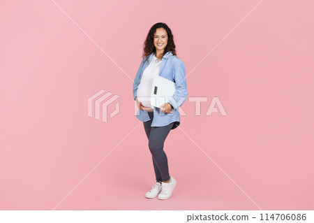 Beautiful pregnant woman holding electronic scales and hugging her big tummy, expecting lady controlling her weight during pregnancy, pink studio background, copy space, full length 114706086