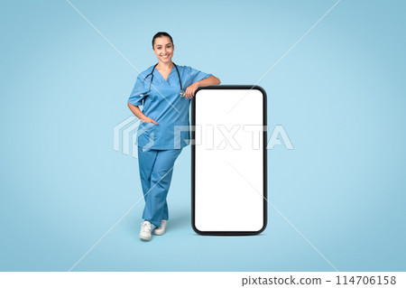 Confident woman nurse leaning on large, blank smartphone mockup for medical app demonstration, dressed in scrubs with stethoscope, on blue backdrop Confident woman nurse leaning on large, blank smartphone mockup for medical app demonstration, dressed in scrubs with stethoscope, on blue backdrop 114706158