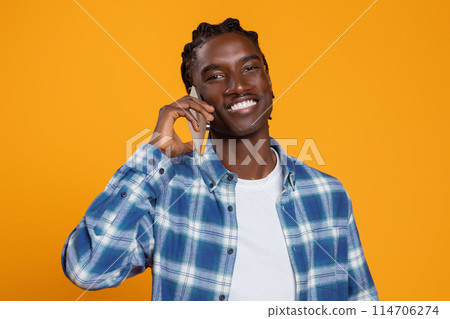 Mobile Communication. Smiling African American Guy Talking On Cellphone And Looking At Camera, Smiling Black Man Enjoying Pleasant Conversation, Standing Isolated On Yellow Background, Copy Space 114706274