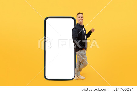 Cool young stylish european guy stand by big phone with white empty screen, showing thumb up and smiling at camera, recommend nice mobile app, mockup, copy space, yellow background Cool young stylish european guy stand by big phone with white empty screen, showing thumb up and smiling at camera, recommend nice mobile app, mockup, copy space, yellow background 114706284