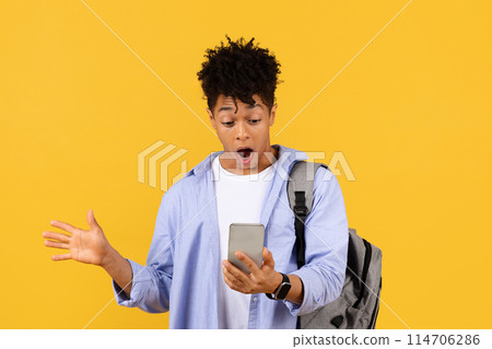 Astonished black male student expresses amazement at his smartphone, wearing backpack, set against bright yellow background, encapsulating moment of unexpected discovery Astonished black male student expresses amazement at his smartphone, wearing backpack, set against bright yellow background, encapsulating moment of unexpected discovery 114706286