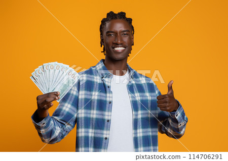 Great Profit. Happy Young Black Man Holding Dollar Cash Money And Showing Thumb Up, Smiling Handsome African American Millennial Guy Recommending Fast Credit, Standing On Yellow Studio Background 114706291