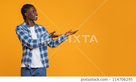 Check This. Smiling Young Black Guy Pointing Aside At Copy Space With Two Palms, Cheerful African American Man Demonstrating Free Place For Advertisement While Standing Isolated On Yellow Background 114706295