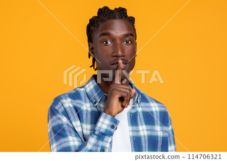 Keep Silence. Portrait Of Young Black Guy Showing Shh Gesture At Camera, Millennial African American Man Holding Finger Near Lips, Gesturing Hush While Standing Isolated On Yellow Studio Background 114706321