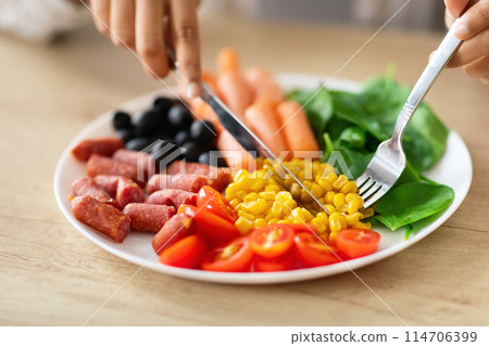 Unrecognizable woman have lunch at kitchen at home, cropped of lady hands holding knife and fork, eating healthy food full of vitamins and minerals, fiber and high in protein meal. Diet, nutrition 114706399