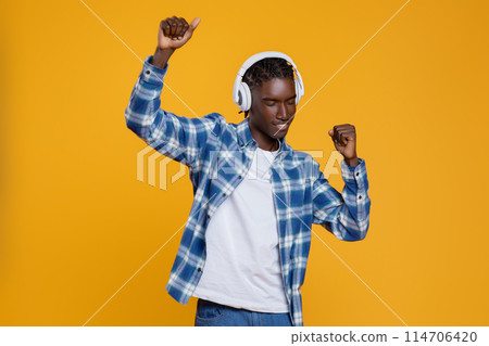 Positive young black man enjoying listening music, dancing and having fun, cheerful millennial african american guy wearing wireless headphones posing on yellow studio background, copy space Positive young black man enjoying listening music, dancing and having fun, cheerful millennial african american guy wearing wireless headphones posing on yellow studio background, copy space 114706420