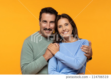 Happy senior european husband and wife in casual clothes hug and looking at camera, isolated on orange studio background. Lifestyle, relationships and love, ad and offer, close up 114706519